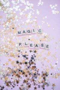 Scrabble letters spell MAGIC PLEASE on lavender background with silver and gold star glitter